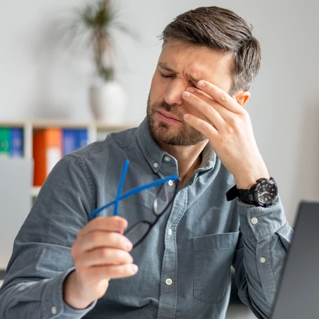 A man at his computer rubbing at his dry, itching eyes